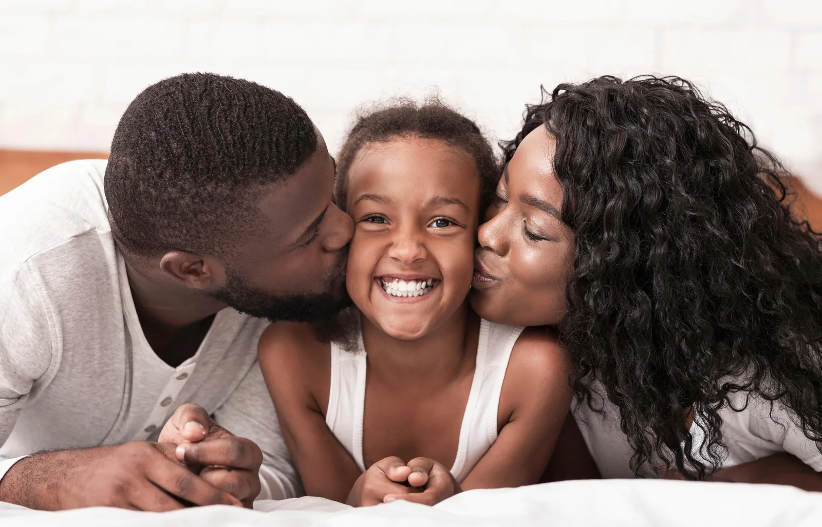 Two parents kissing their smiling daughter on the cheeks