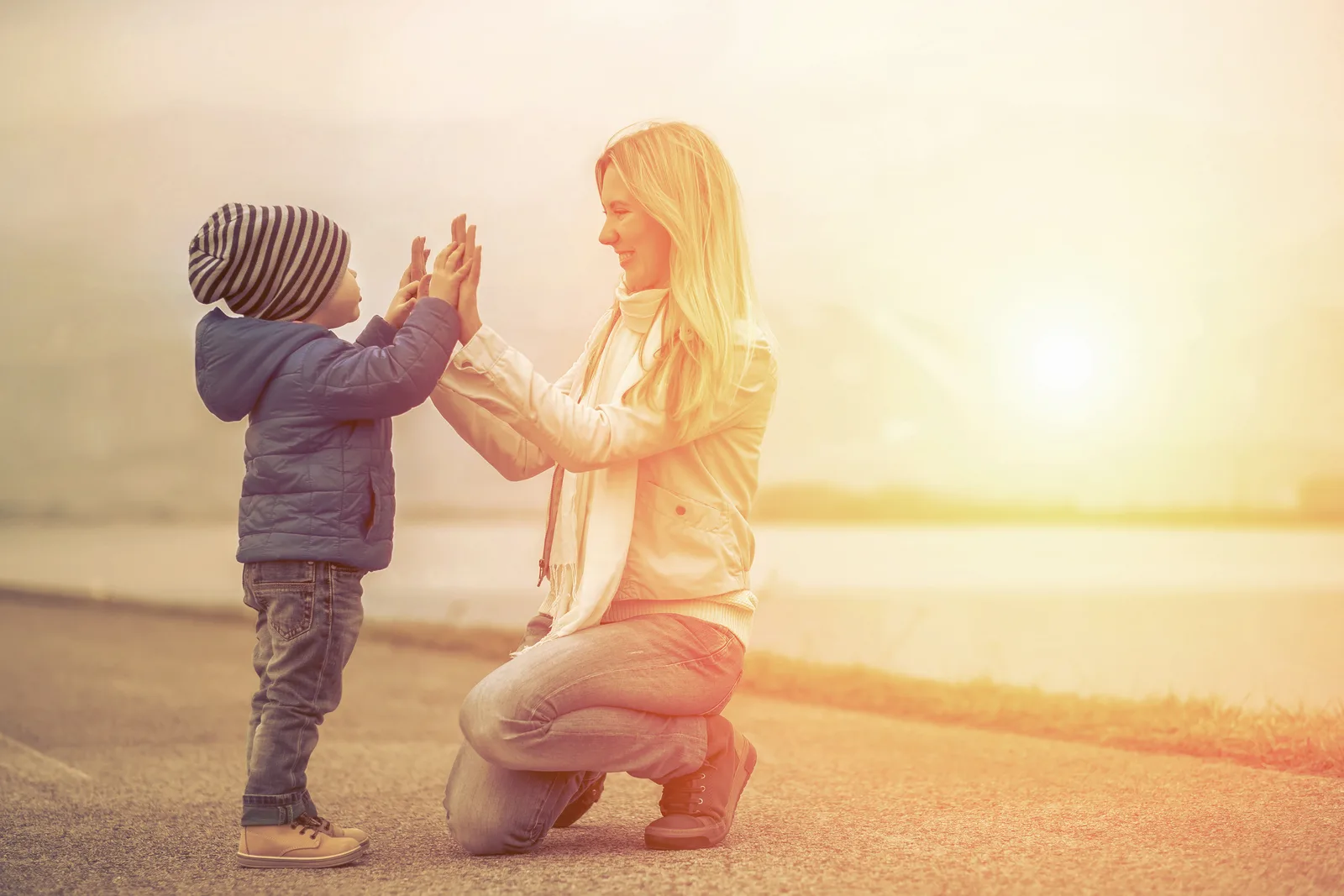 A mother kneeling to high-five her young son at sunset by the water